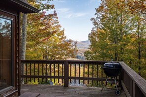 A wooden deck with a barbecue grill, overlooking a forested area with autumn foliage.