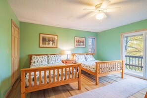 A bedroom with two wooden beds, a ceiling fan, and a window with a view of trees.