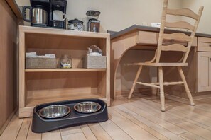 A kitchen with wooden cabinets, a coffee maker, a kettle, and a pet feeding station.
