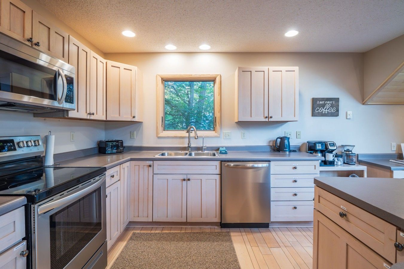 A modern kitchen with stainless steel appliances, a window, and a coffee station.