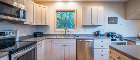 A modern kitchen with stainless steel appliances, a window, and a coffee station.