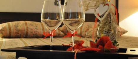 A tray with two wine glasses, a bottle of champagne, and a heart-shaped decoration on a bed with floral-patterned bedding.