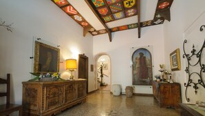 Ett rymligt rum med ett polerat stengolv, möbler i trä och ett tak med färgstarka, geometriska mönster.