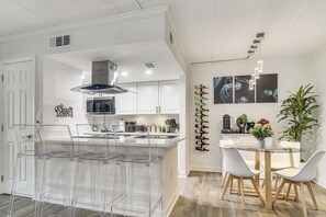 A modern kitchen with a central island, bar stools, a dining table with chairs, and a wall-mounted wine rack. - < 2 Mi to Coast: St Pete Beach Gem w/ Pool Access (St Pete Beach)