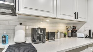 Een keuken met witte kastjes, een koffiezetapparaat, een broodrooster en een aanrecht met diverse spullen.
