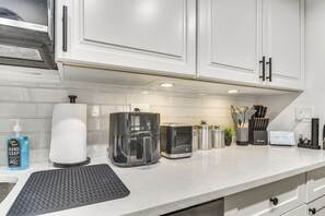 Une cuisine avec des meubles blancs, une machine à café, un grille-pain et un plan de travail sur lequel se trouvent divers objets.