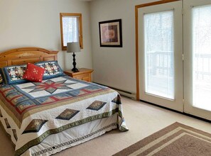 A bedroom with a bed, a nightstand, a lamp, a framed picture, and a window with blinds. - Zigadeaux - Hot Tub, Wood Burning Fireplace (Davis)