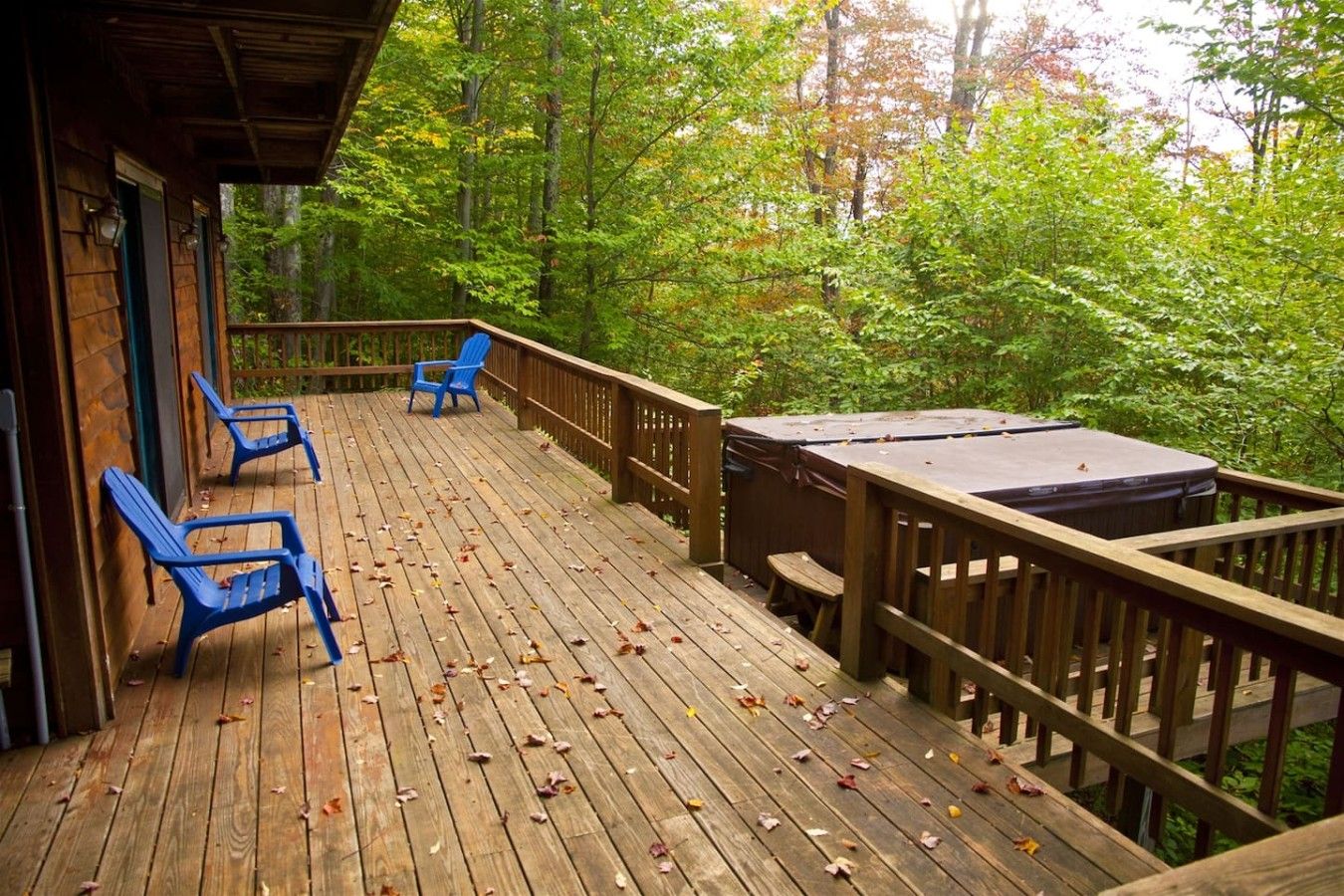 A wooden deck with a hot tub, chairs, and a view of a forest.