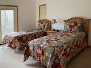 Two single beds with wooden headboards, a bedside table with a lamp, and a window with blinds.