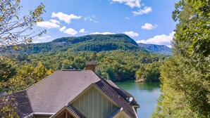 Ein Haus mit einem geneigten Dach, einem Steinkamin und Blick auf einen See, der von bewaldeten Hügeln umgeben ist.