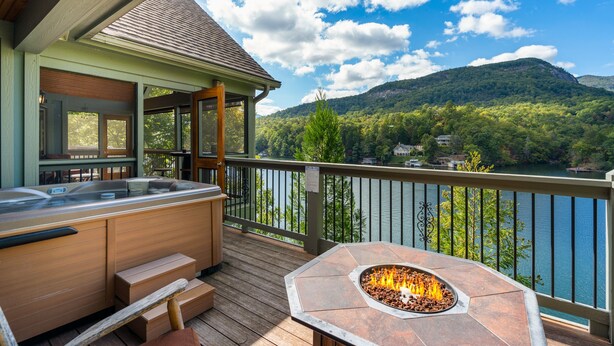 Eine Terrasse mit Whirlpool und Feuerstelle, mit Blick auf einen See und Berge.