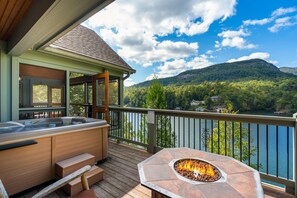 A deck with a hot tub and a fire pit, overlooking a lake and mountains. - Over the Edge - Lakefront, Hot tub, Sleeps 10, Two kayaks (Lake Lure)