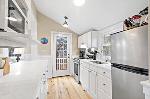 A kitchen with white cabinets, a stainless steel refrigerator, a stove, and a window with a view of trees.