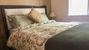 A bed with a floral-patterned bedspread, a headboard, and a window with daylight. - Talkeetna's Mount Dall Cottage - WiFi&laundry - easy access from Parks Highway! (Talkeetna)