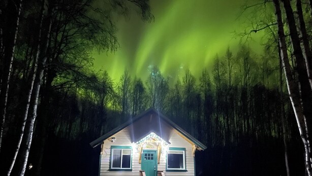 A small cabin with a green door, two chairs outside, and a staircase leading up to the entrance. - Talkeetna's Mount Dall Cottage - WiFi&laundry - easy access from Parks Highway! (Talkeetna)