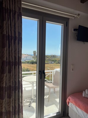 Ein Zimmer mit einem Bett, einem an der Wand montierten Fernseher und einer Glastür, die zu einem Außenbereich mit Tisch und Stühlen führt.