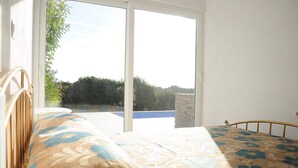 Un dormitorio con cama, ventana y vista a una piscina y follaje.