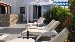 Un patio con sillones de descanso y una sombrilla blanca.