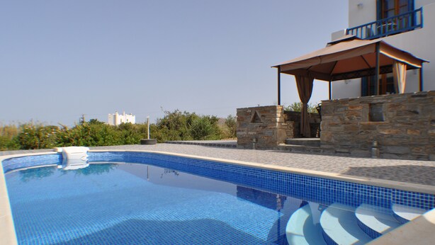Una piscina con un muro de piedra y un área de patio techada.