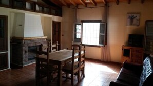 A room with a fireplace, a dining table with chairs, a window with curtains, and a television on a cabinet. - HOUSE OF LA VIÑA, ALMACHAR 8 PERS (Almáchar)