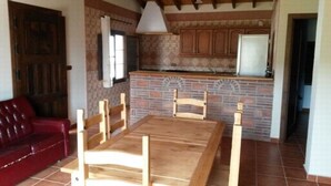 A dining area with a wooden table and chairs, a red sofa, and a kitchen with brick walls and wooden cabinets. - HOUSE OF LA VIÑA, ALMACHAR 8 PERS (Almáchar)