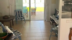 Een kamer met een eethoek, een zithoek met stoelen, een televisie en uitzicht op het omliggende landschap.