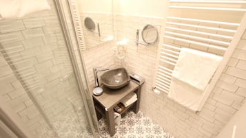 A small bathroom with a glass shower enclosure, a sink with a vessel basin, and a towel rack.
