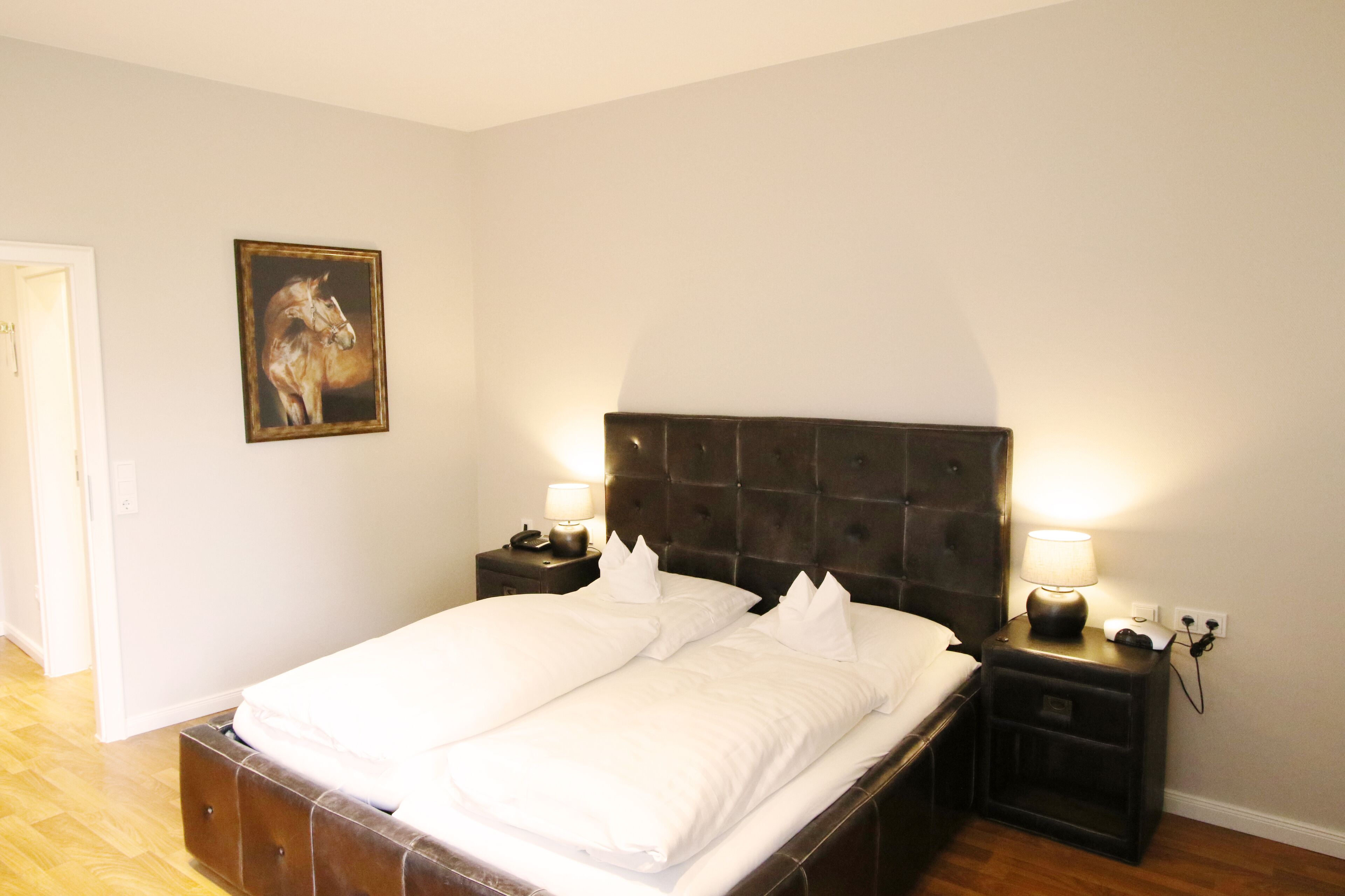 Un dormitorio con una cama grande, dos mesitas de noche con lámparas, un aparador y un cuadro enmarcado en la pared.