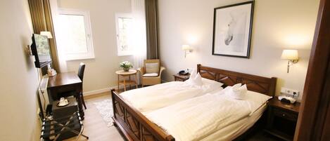 A hotel room with a double bed, a desk with a chair, a small table with a plant, and two wall-mounted lamps.