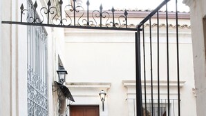 Una entrada estrecha con puerta de madera, rejas metálicas y un felpudo de cerámica que da a un balcón.
