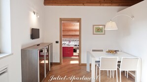 Un apartamento moderno con techo de madera, una cocina con armarios rojos, una zona de comedor con mesa y sillas blancas, y un televisor montado en la pared.