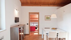 A modern apartment with a wooden ceiling, a kitchen with red cabinets, a dining area with a white table and chairs, and a TV mounted on the wall.