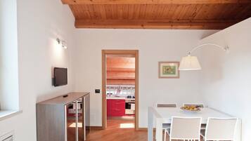 A modern apartment with a wooden ceiling, a kitchen with red cabinets, a dining area with a white table and chairs, and a TV mounted on the wall.