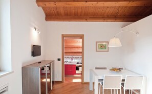 A modern apartment with a wooden ceiling, a kitchen with red cabinets, a dining area with a white table and chairs, and a TV mounted on the wall. - SICILY ROMANTIC CHARMING APARTMENT IN THE HEART OF MODICA'S HISTORICAL CENTER! (Modica)