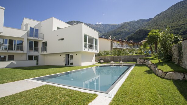 Ein modernes Haus mit Schwimmbad, einem gepflegten Rasen und Bergen im Hintergrund.