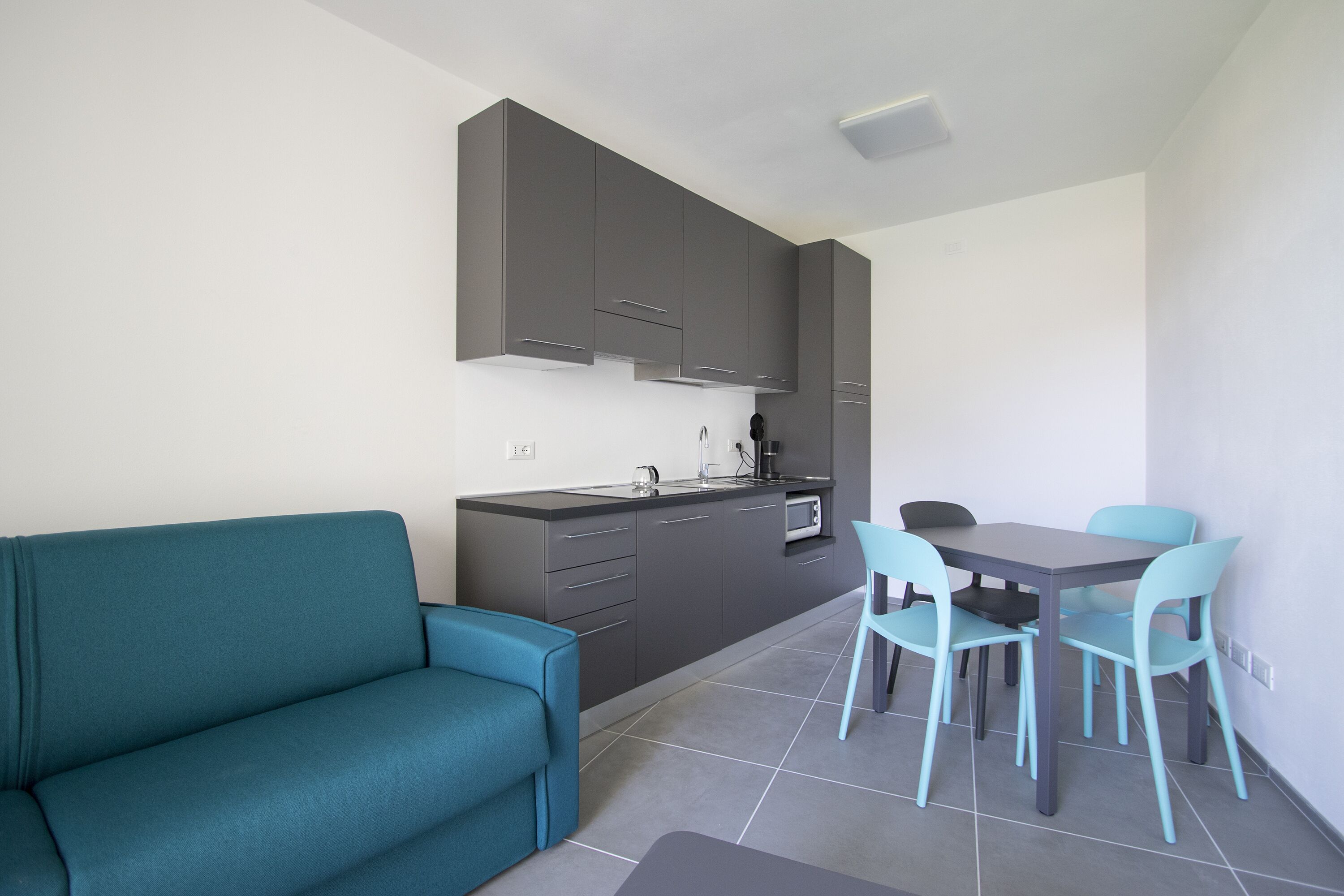 Une cuisine de taille réduite avec des meubles gris, un canapé de couleur turquoise et une table à manger avec quatre chaises.
