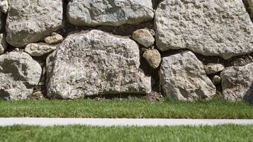Un mur de pierres, composé de gros blocs, avec une zone herbeuse devant.