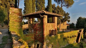 Une ancienne construction en pierre, dont les murs sont recouverts de lierre et le toit en bois, entourée d’arbres et bordée d’un sentier pavé.