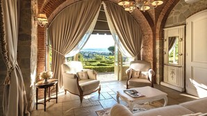 Une chambre luxueuse avec une arche en pierre, deux fauteuils confortables, une table basse et une vue sur un vignoble.