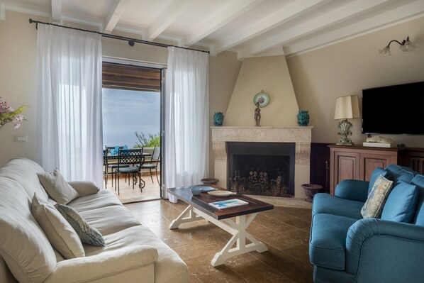 A living room with a sofa, a blue armchair, a fireplace, a television, and a dining area with a table and chairs.