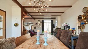 A wooden dining table with two candles, a chandelier, and a view into a kitchen and living area.
