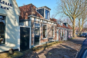 Traditional Dutch building with a brick facade and red-tiled roof, featuring windows with shutters and a small porch.