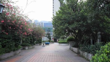 A paved pathway flanked by greenery and a tall building in the background.