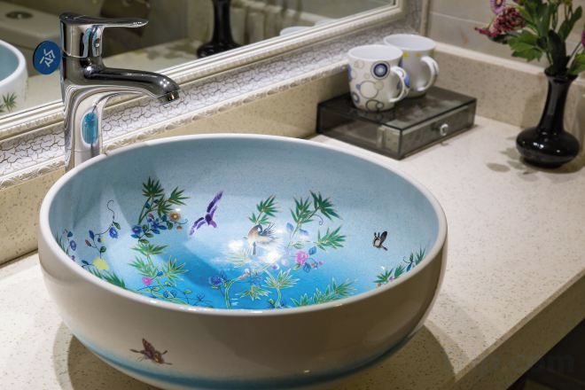 A bathroom with a large, round, blue ceramic sink with plant designs.