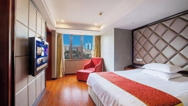 Une chambre d’hôtel avec un lit, une télévision, un fauteuil rouge et une vue sur la ville.