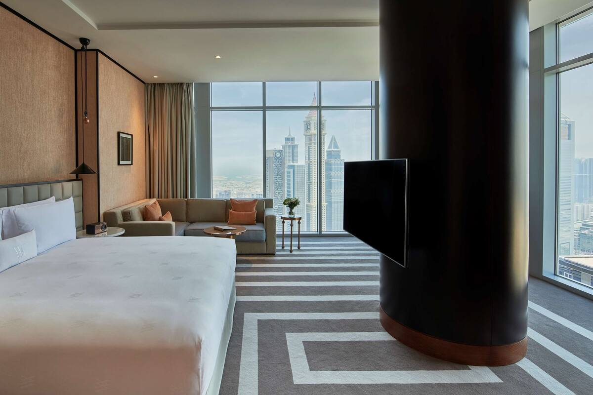A hotel room with a large bed, a sofa, a TV, and a view of the city skyline.