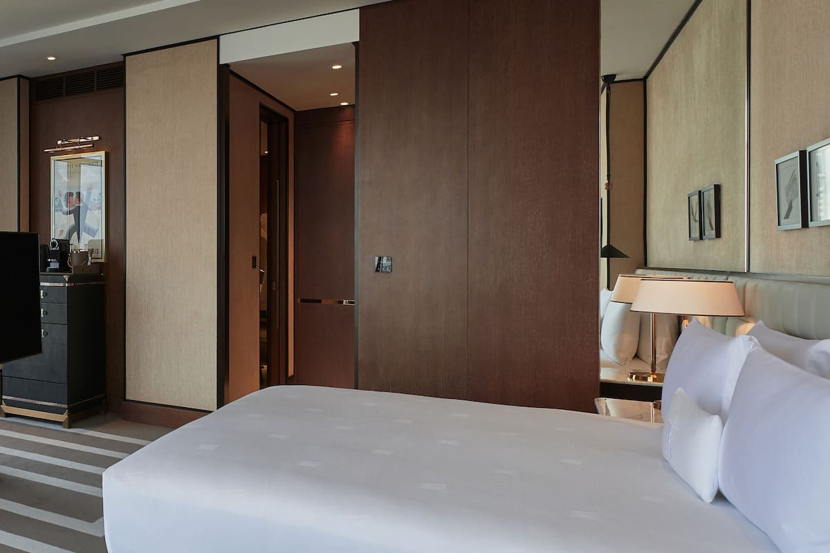 A modern hotel room with a large bed, a desk with a computer, a lamp, and a wall-mounted TV.