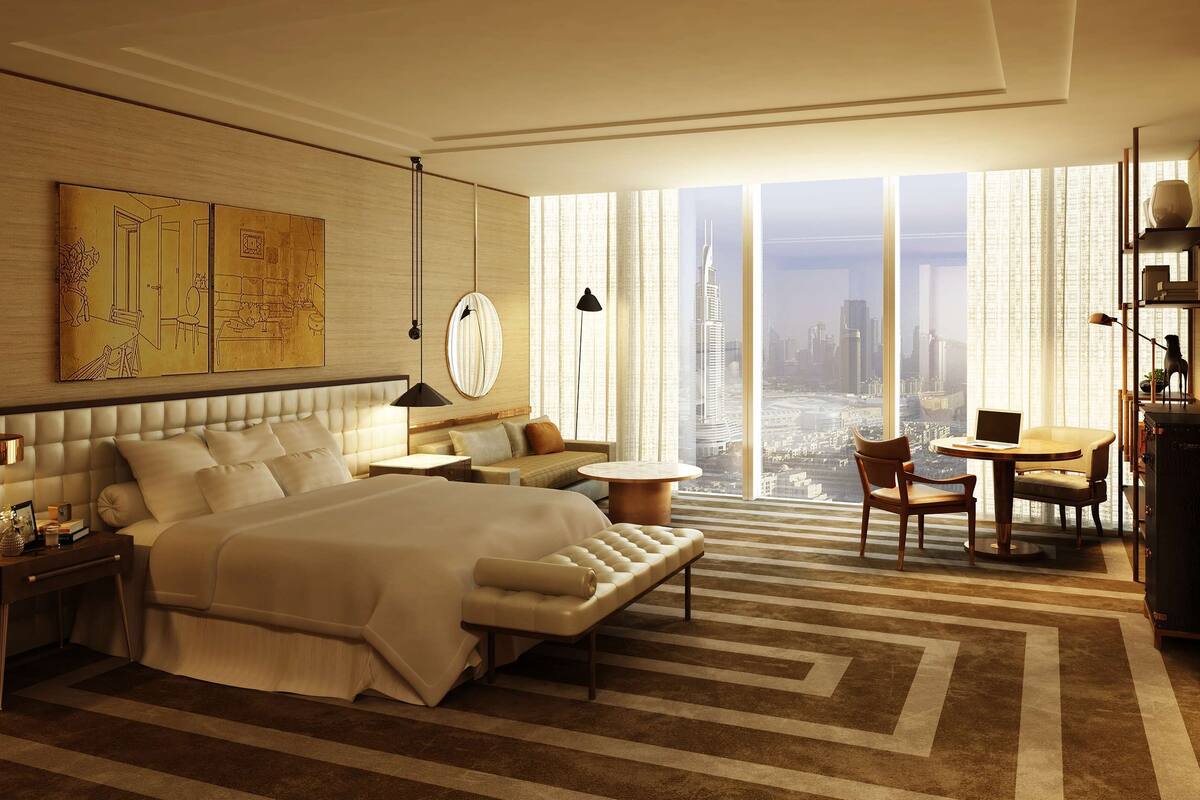 A modern hotel room with a large bed, a sofa, a dining table, and a view of a cityscape through floor-to-ceiling windows.
