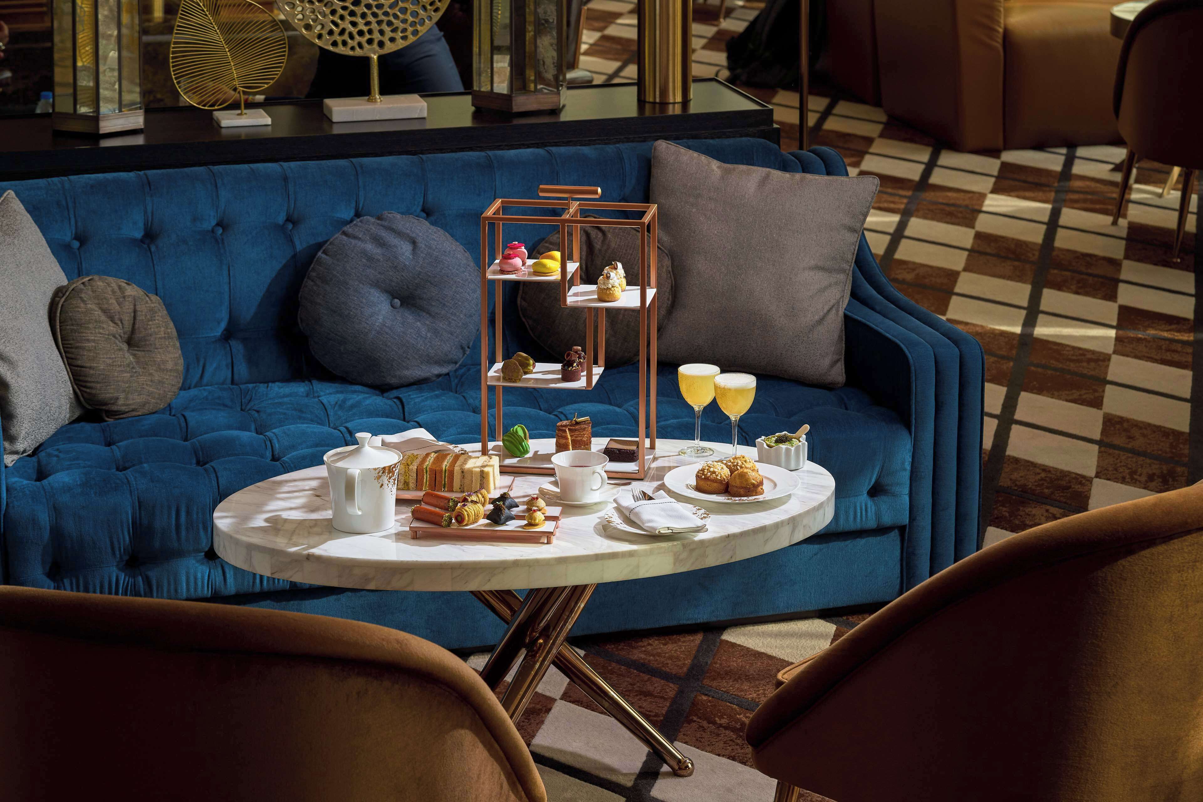 A blue sofa with a round table in front, featuring a tray with pastries and drinks.