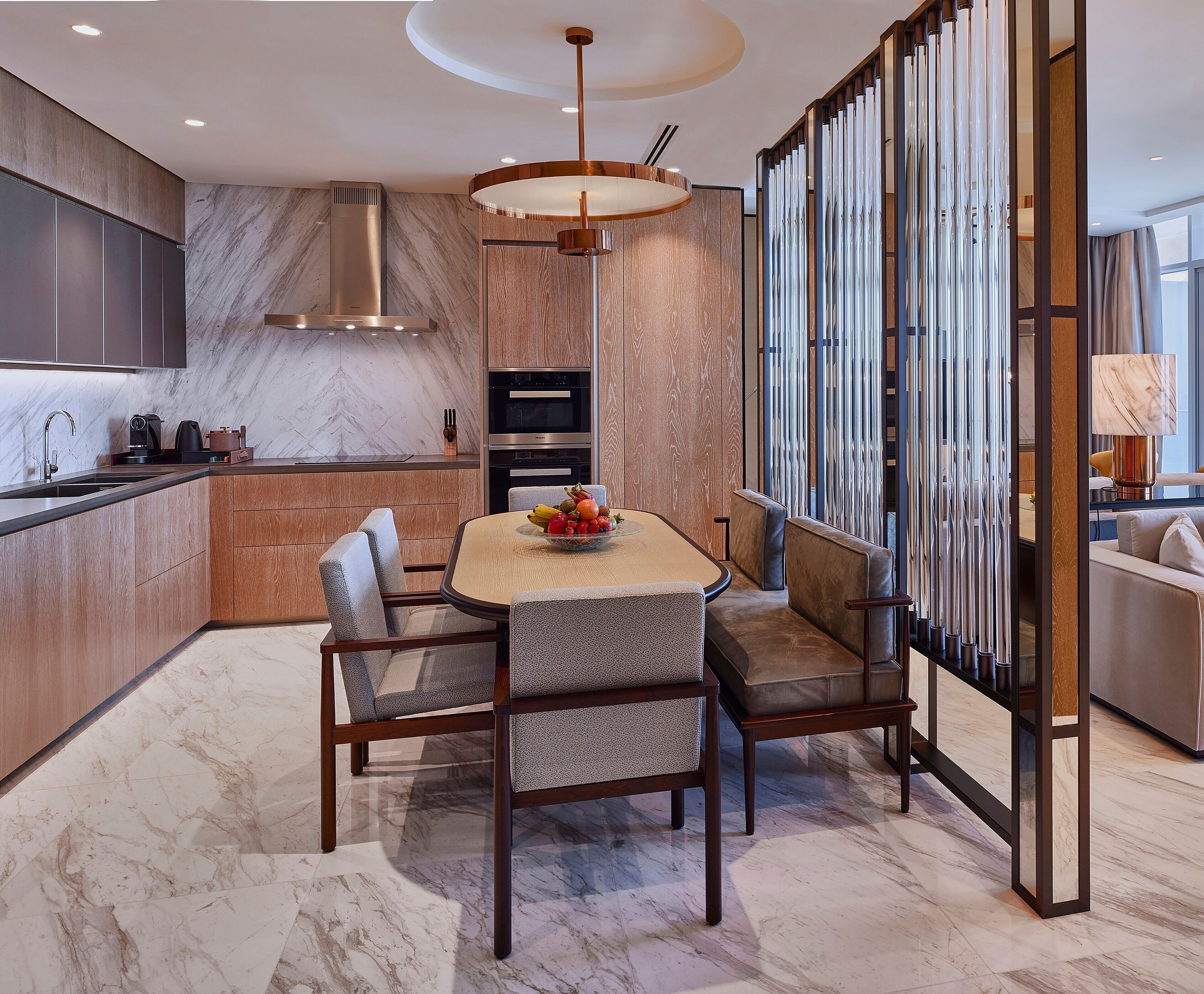 Una cocina moderna con encimera de mármol, electrodomésticos integrados y un comedor con mesa de mármol y sillas acolchadas.